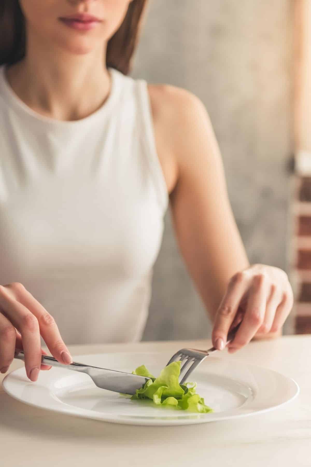 woman with eating disorder cutting a piece of lettuce.