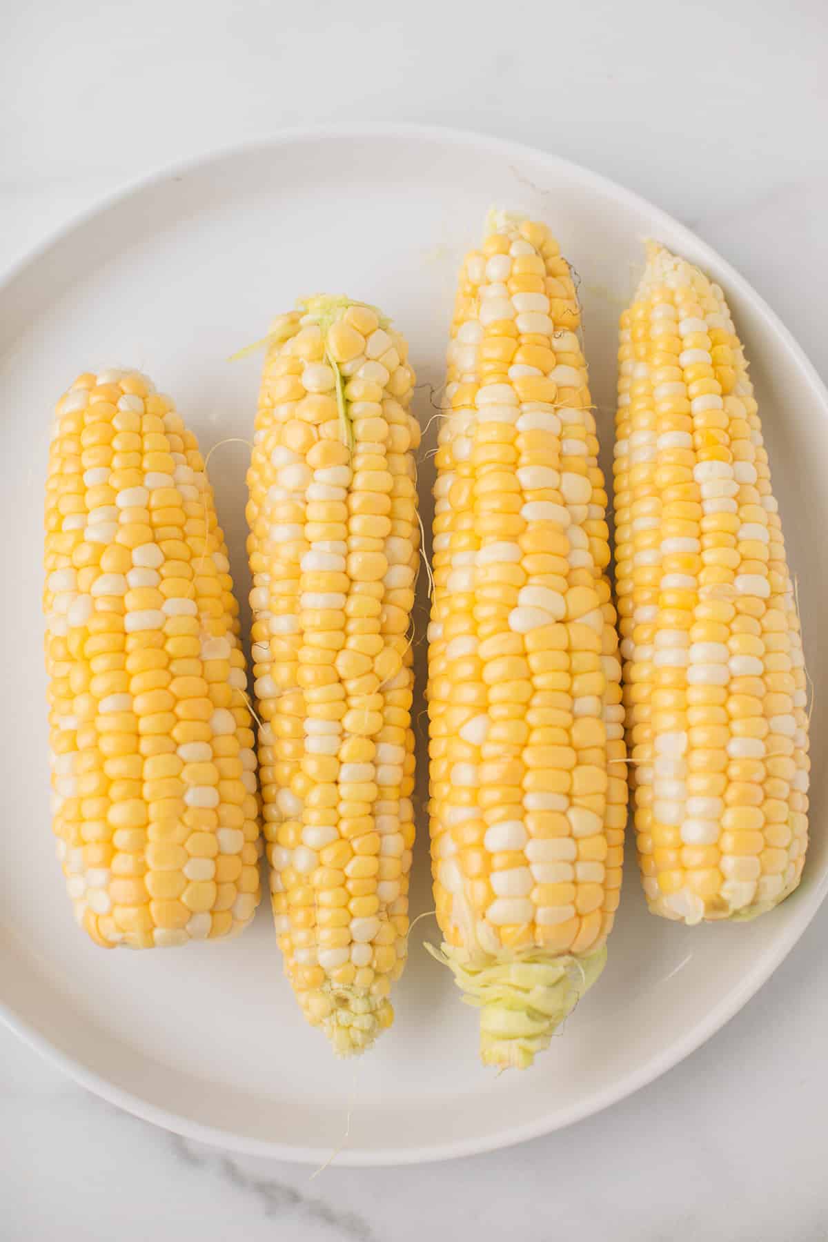 four pieces of corn on a plate with the corn husks removed.