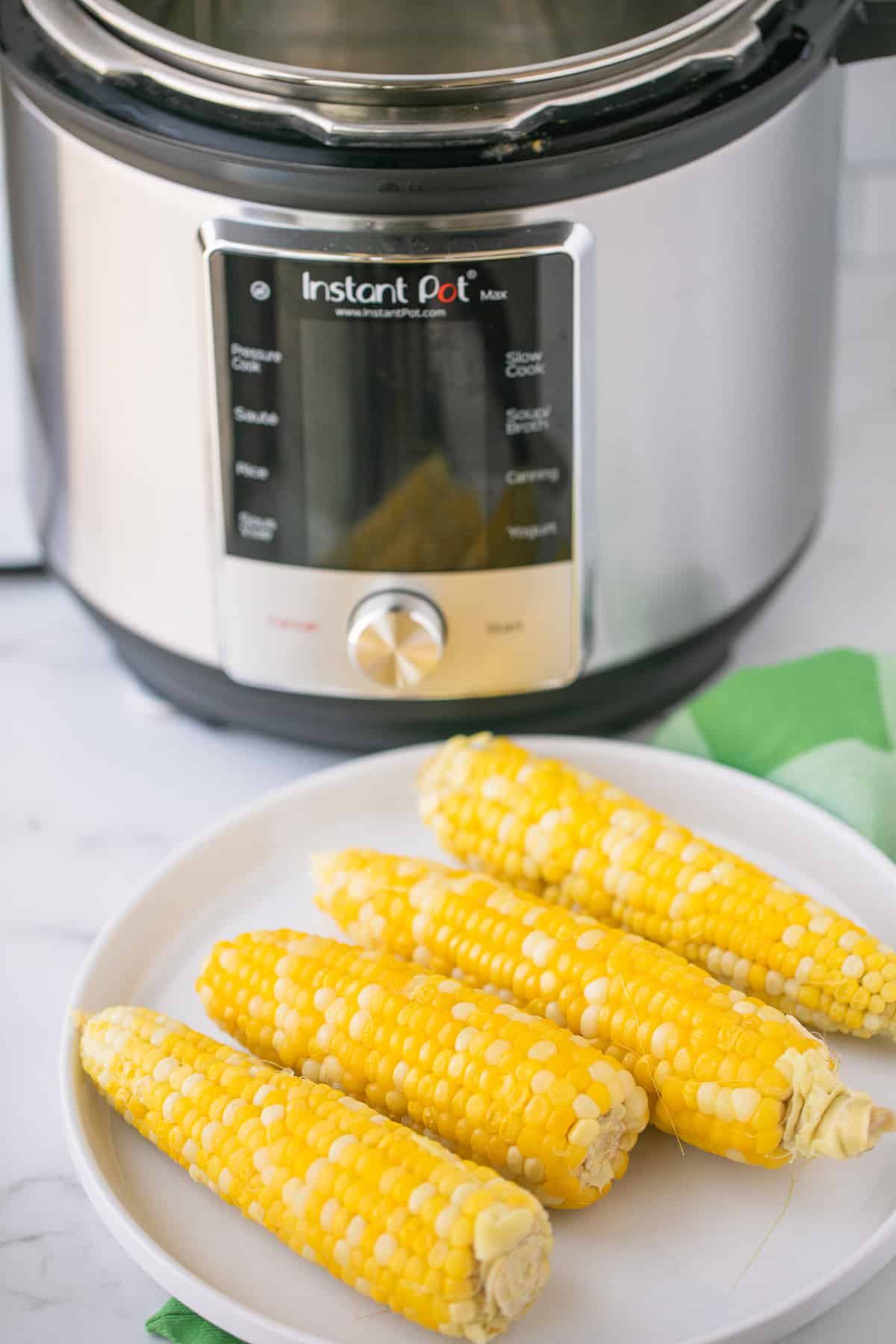 plate of cooked corn on the cob in front of an instant pot pressure cooker.