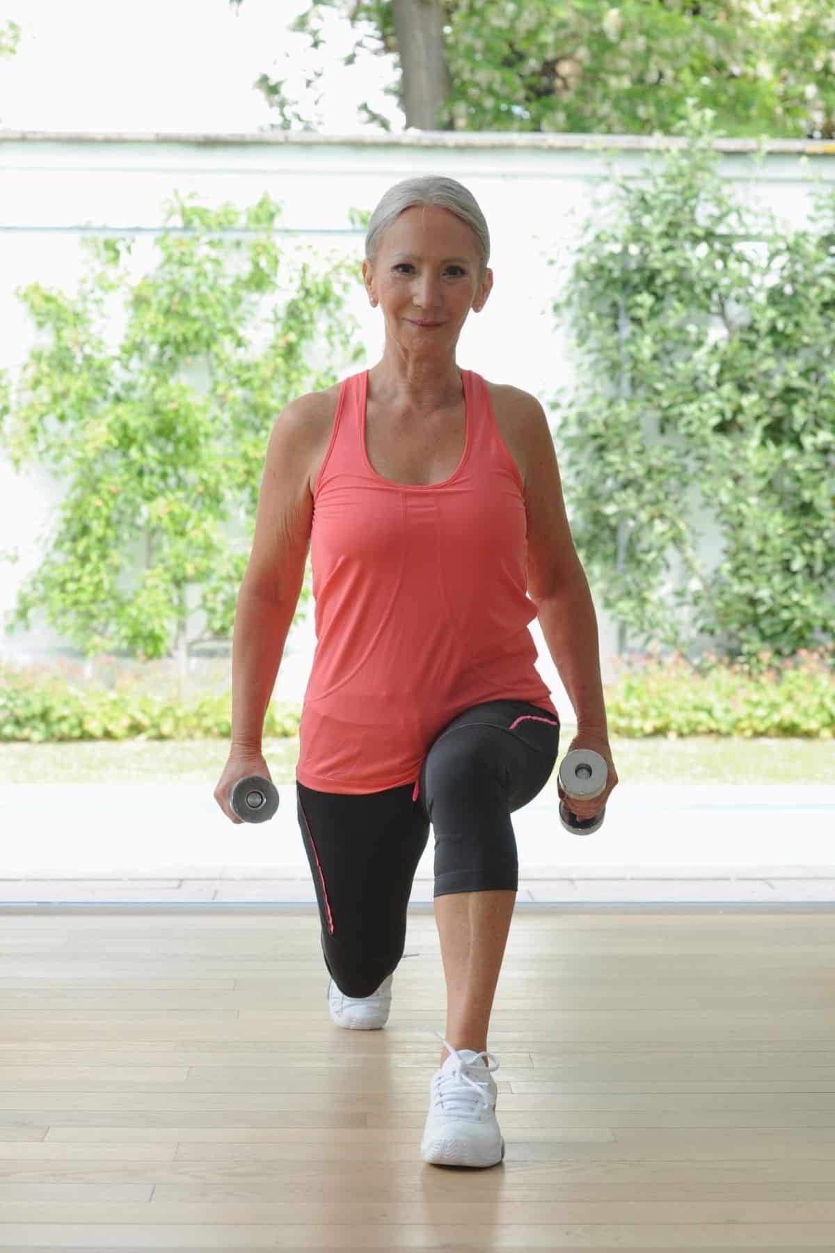 older woman doing lunges with dumbbells in each hand.