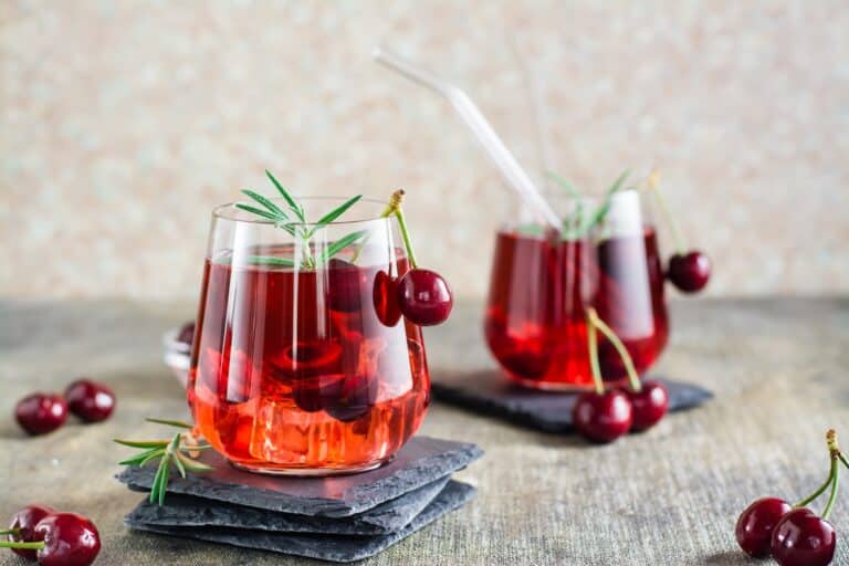 cherry mocktail on table garnished with cherries and rosemary.