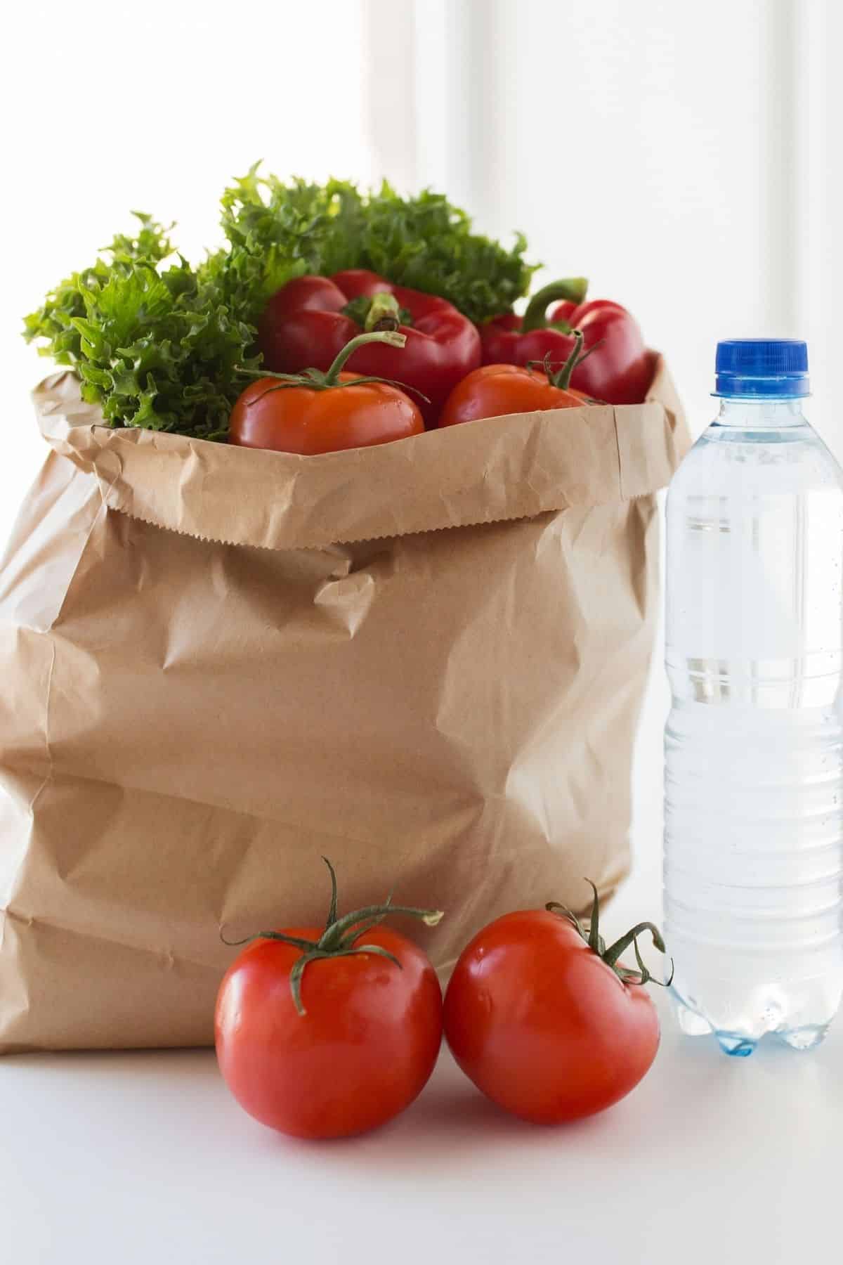 vegetables in grocery bag on a countertop with a bottle of water.