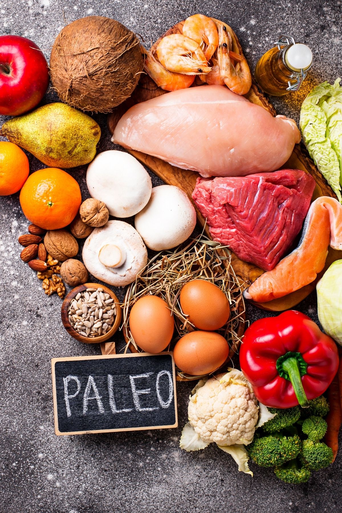 paleo diet foods on a table including meats, vegetables, fish, and eggs.
