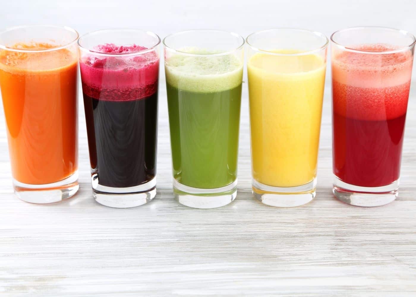 five colorful vegetable and fruit juices lined up on a table.