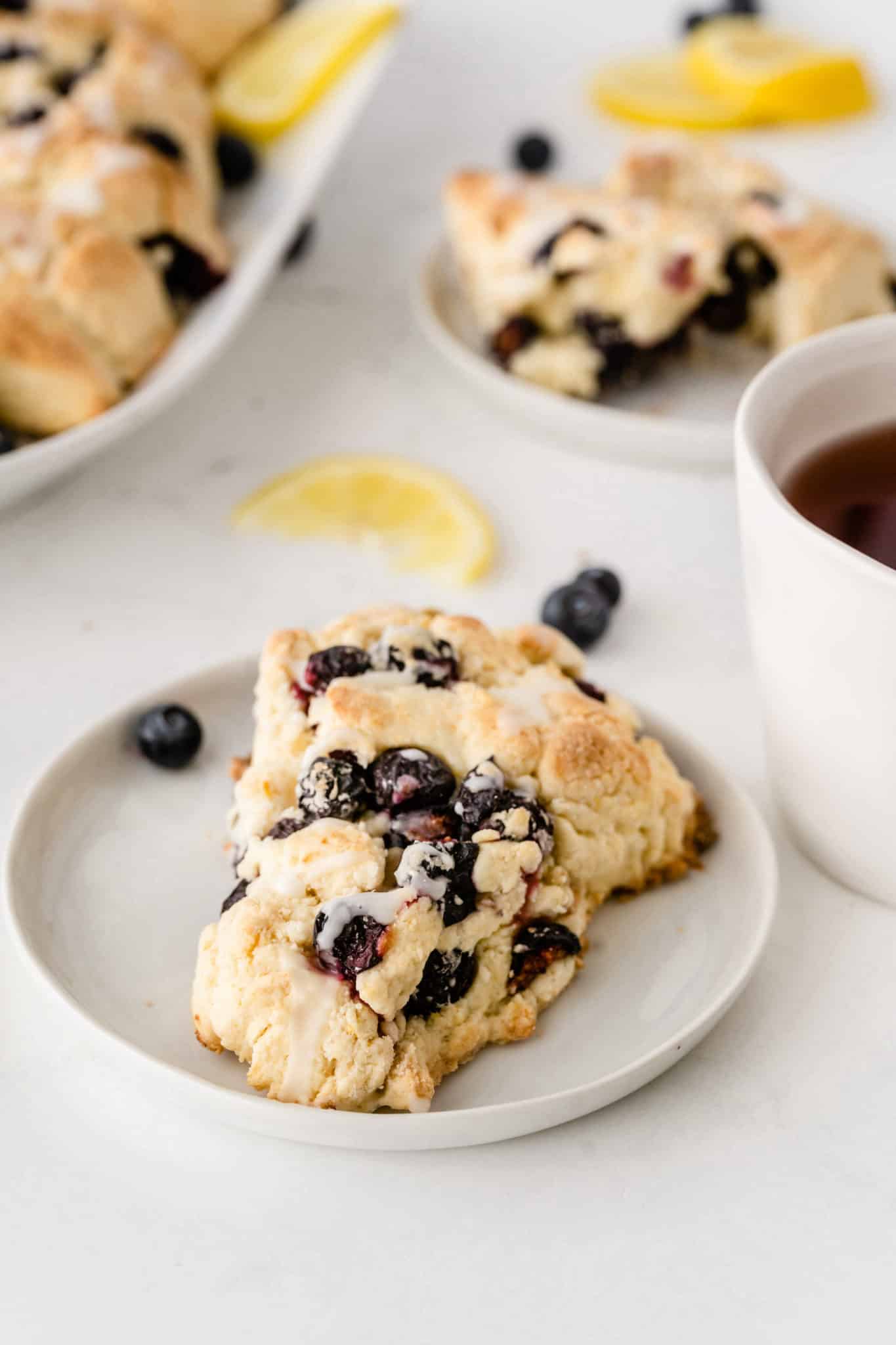 blueberry scone served on a plate with fresh blueberries and a cup of tea.