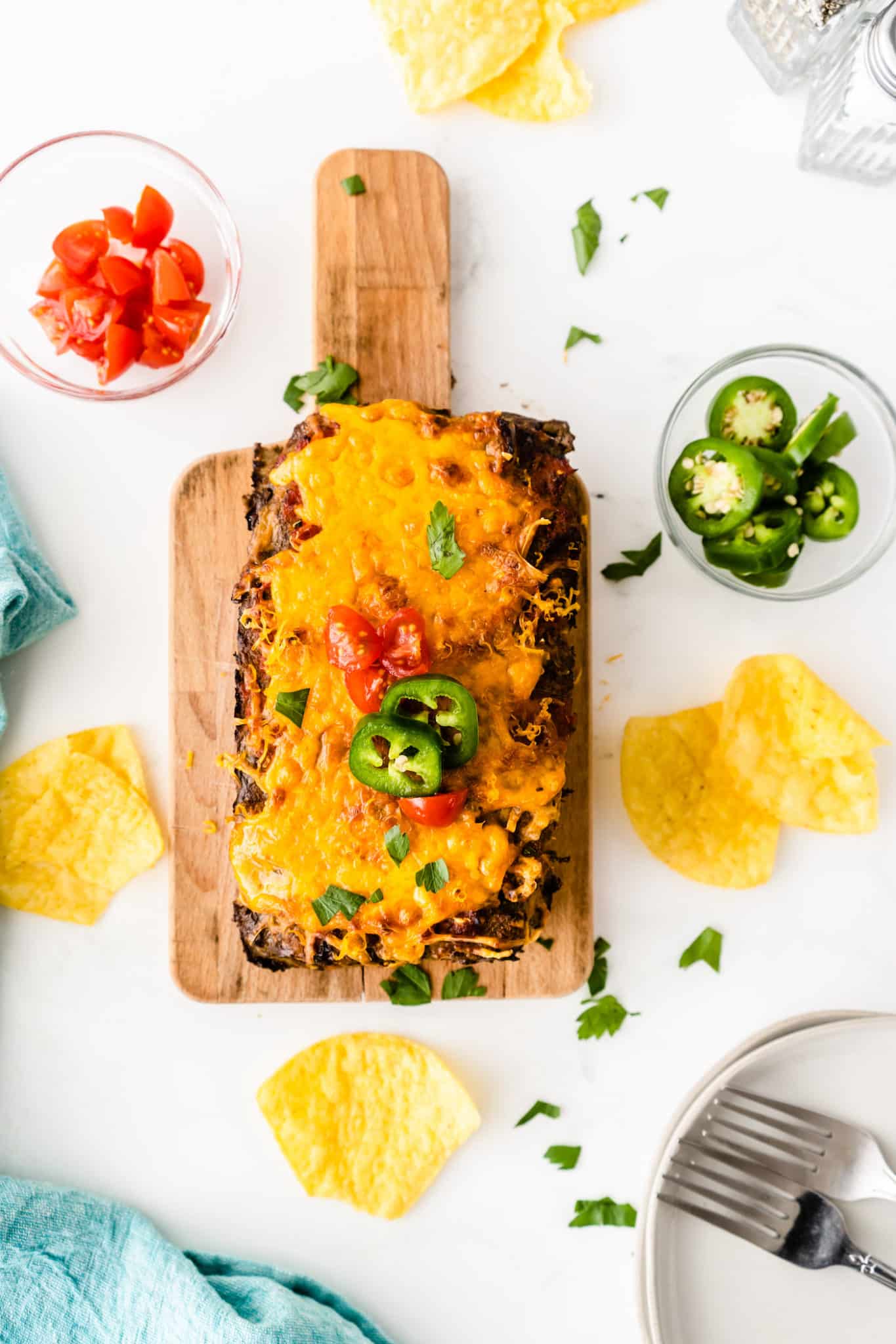 cooked taco meatloaf served on a wooden cutting board with extra toppings.