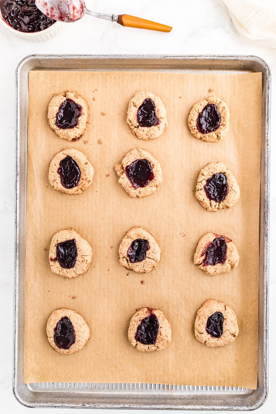 jam-filled thumbprint cookies on a baking sheet for oven.