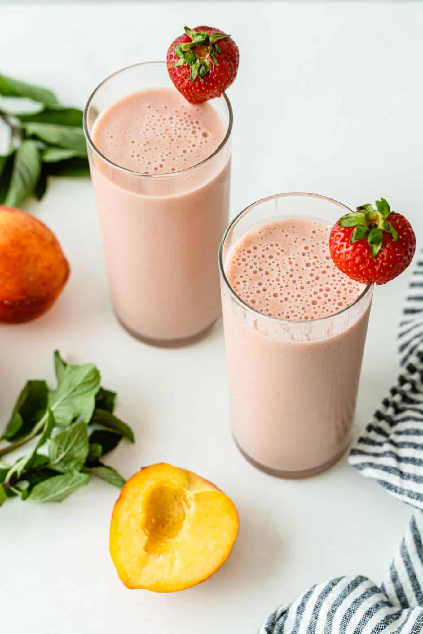 two glasses of strawberry peach smoothies garnished with strawberries.