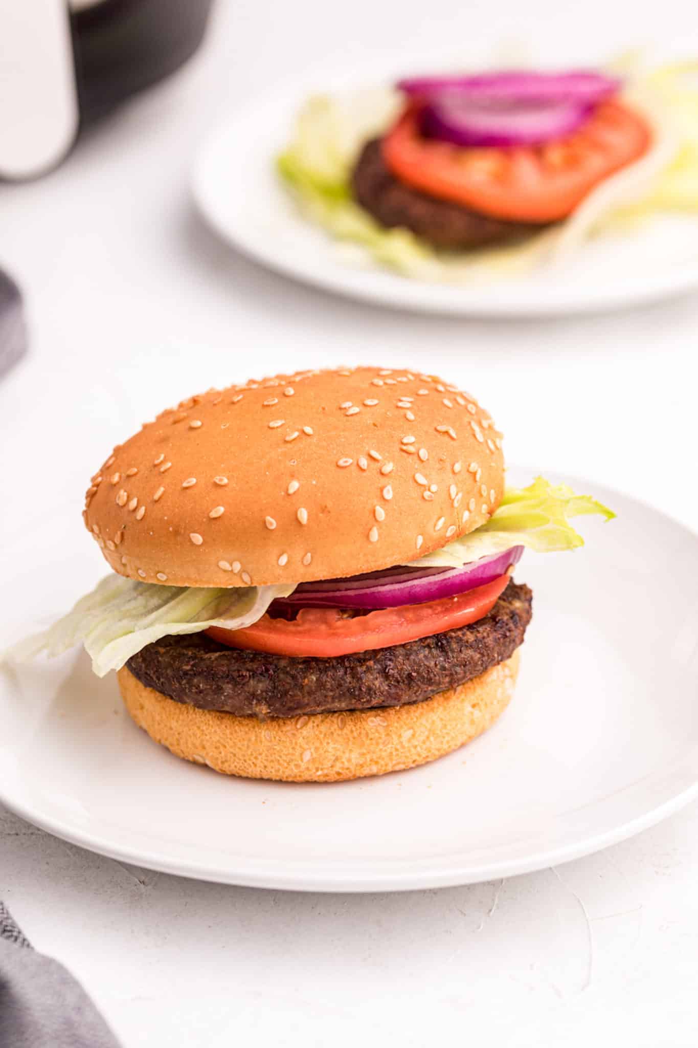 An air fryer cooked hamburger with onion and tomato.