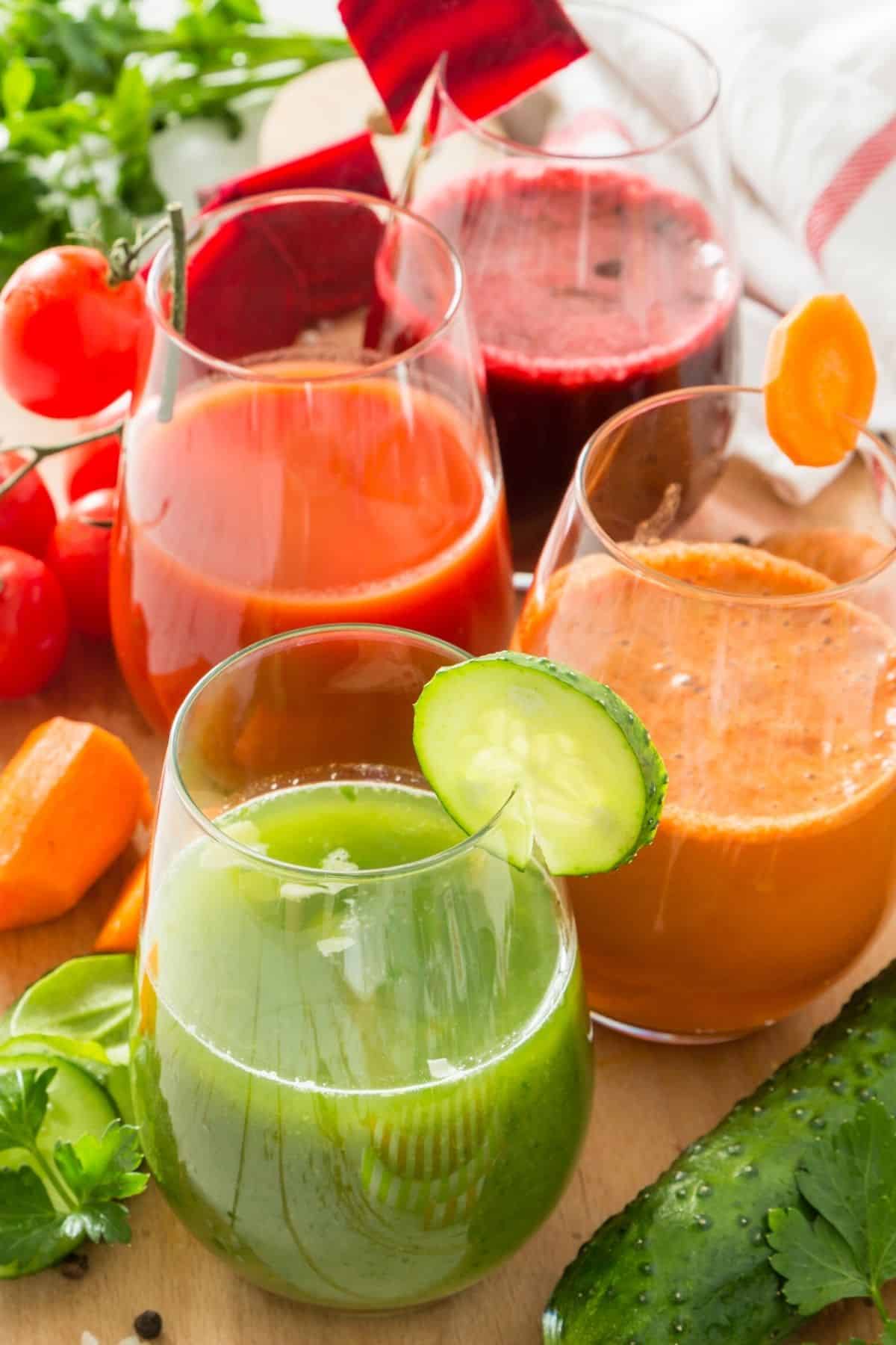 three cups of colorful fresh fruit and vegetable juices on a table.