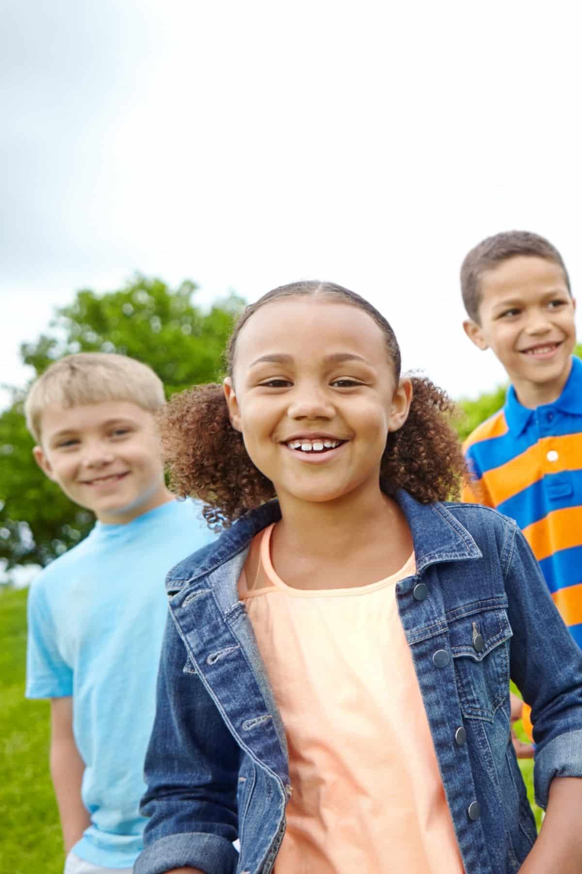 three smiling children at a park.