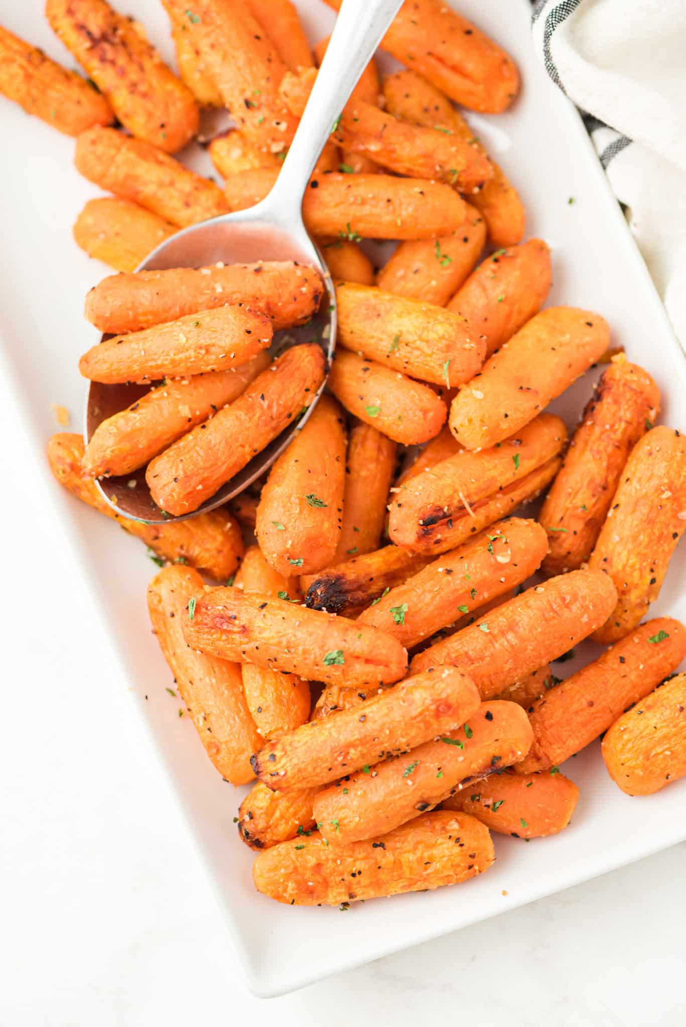 cooked baby carrots on a serving plate with spoon