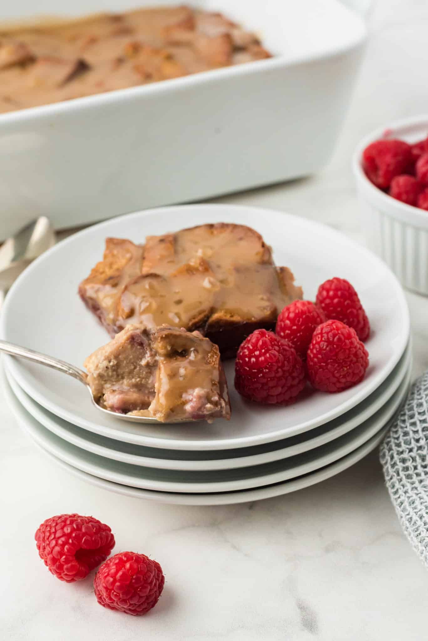 bread pudding served on a white plate with raspberries.