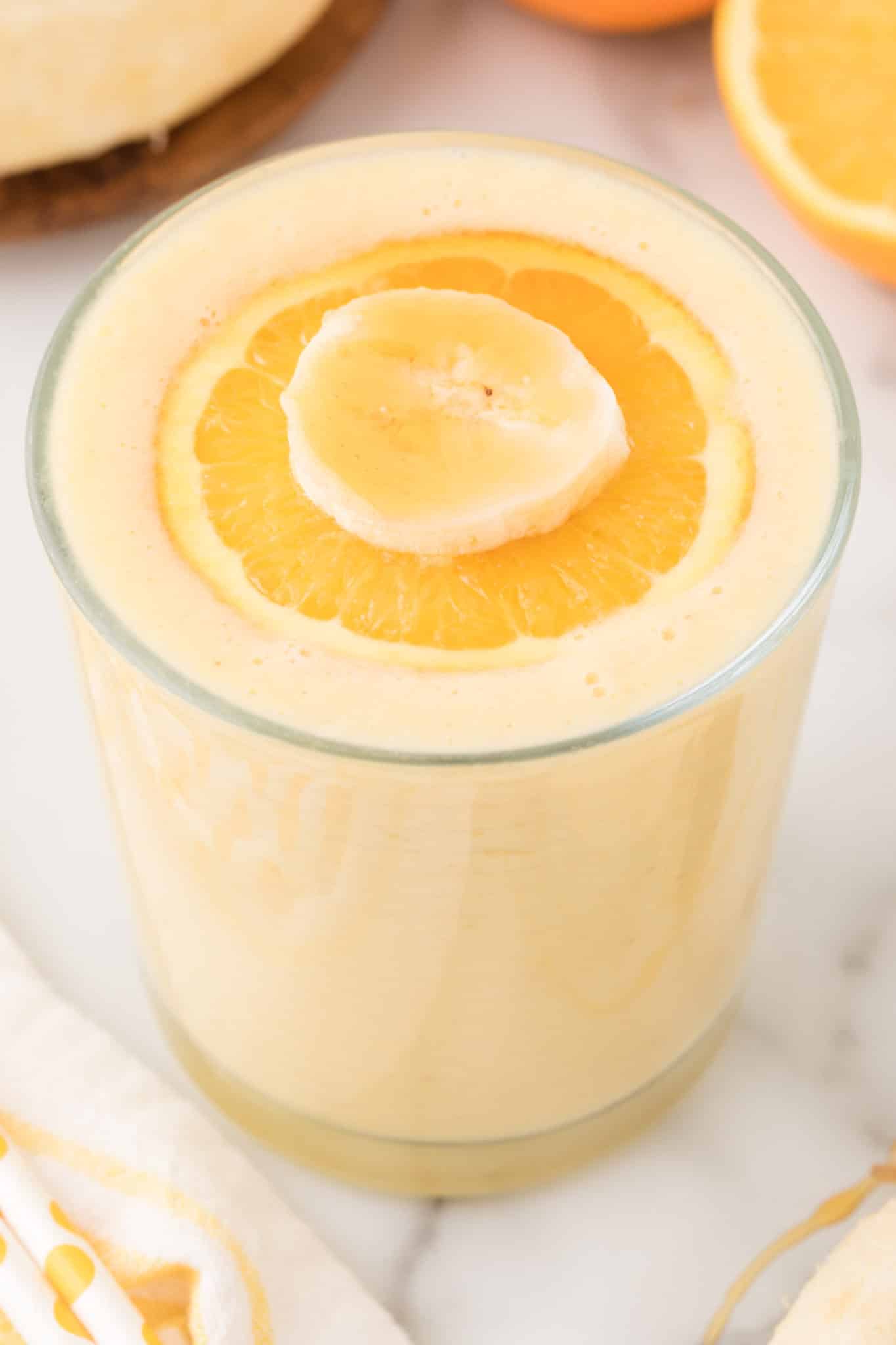 orange banana smoothie in glass topped with orange slice.