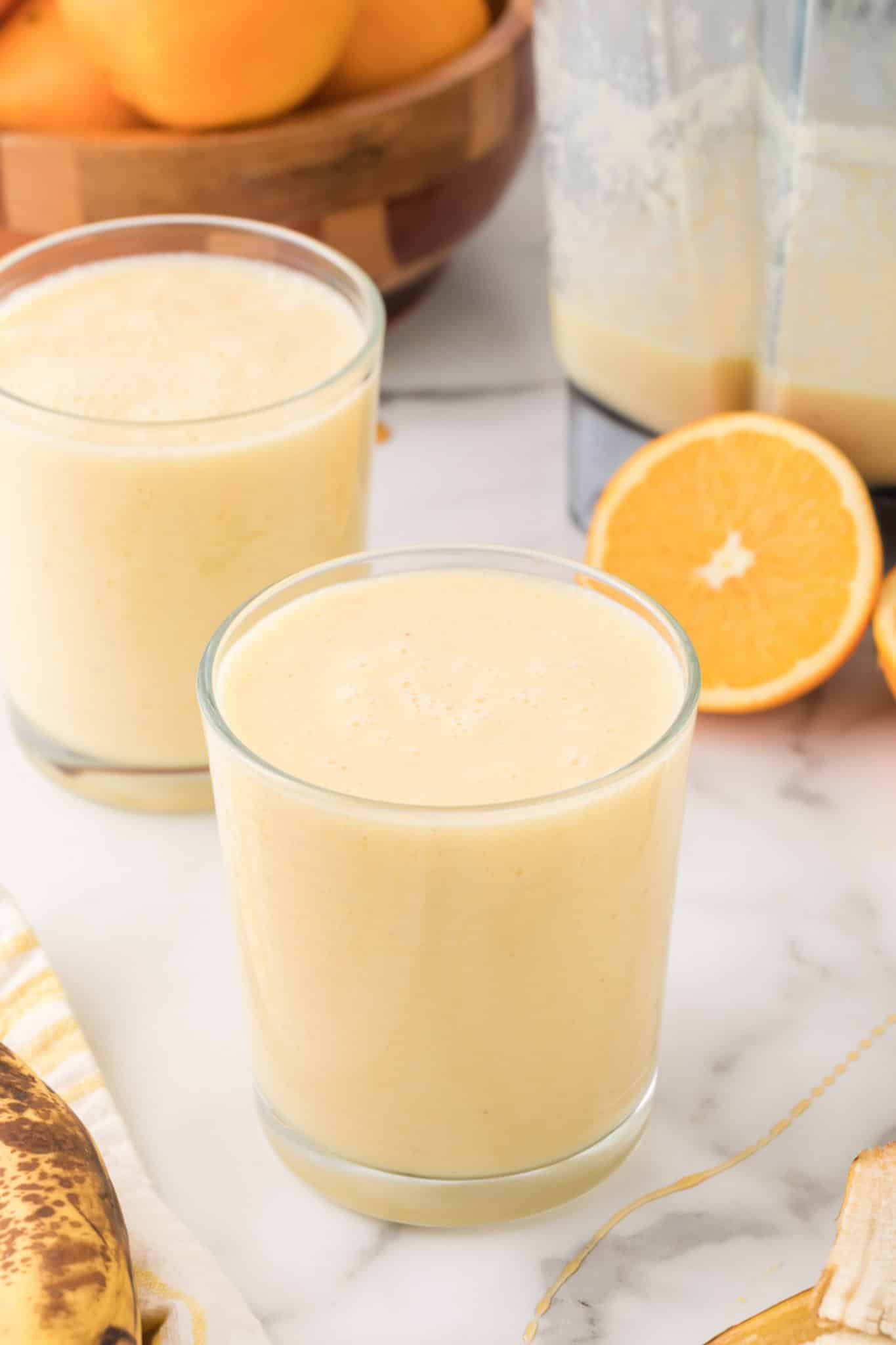 two glasses of orange smoothie on table.