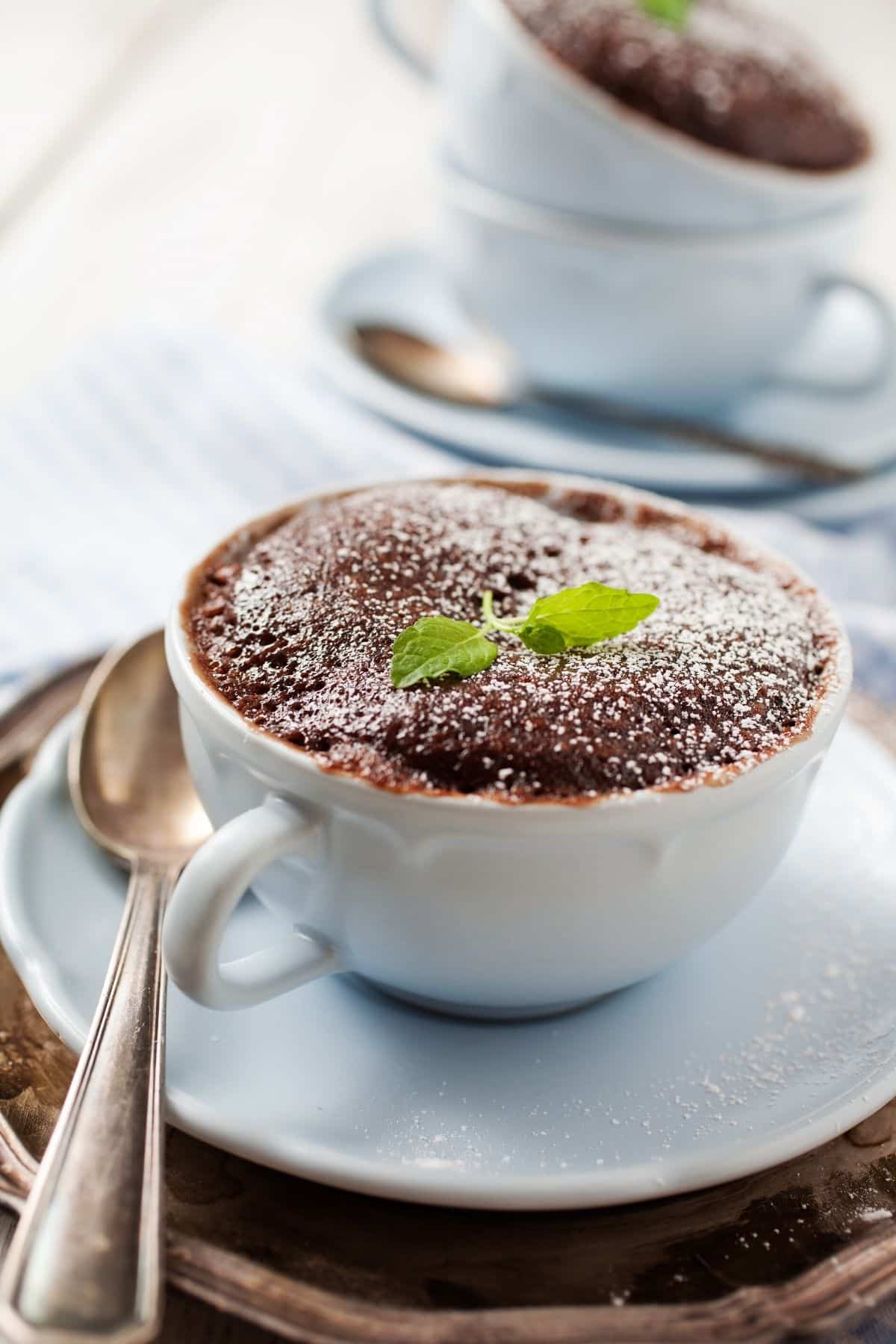 chocolate mug cake on table with powdered sugar on top.