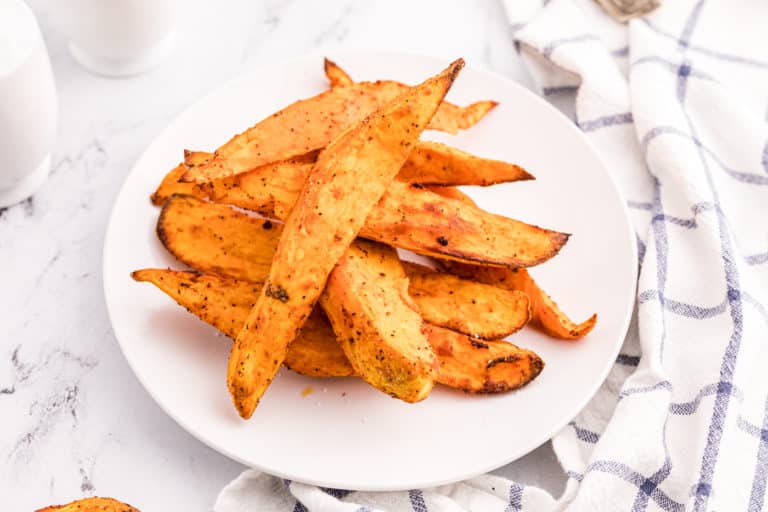 Air fryer sweet potato wedges piled up on a white plate.