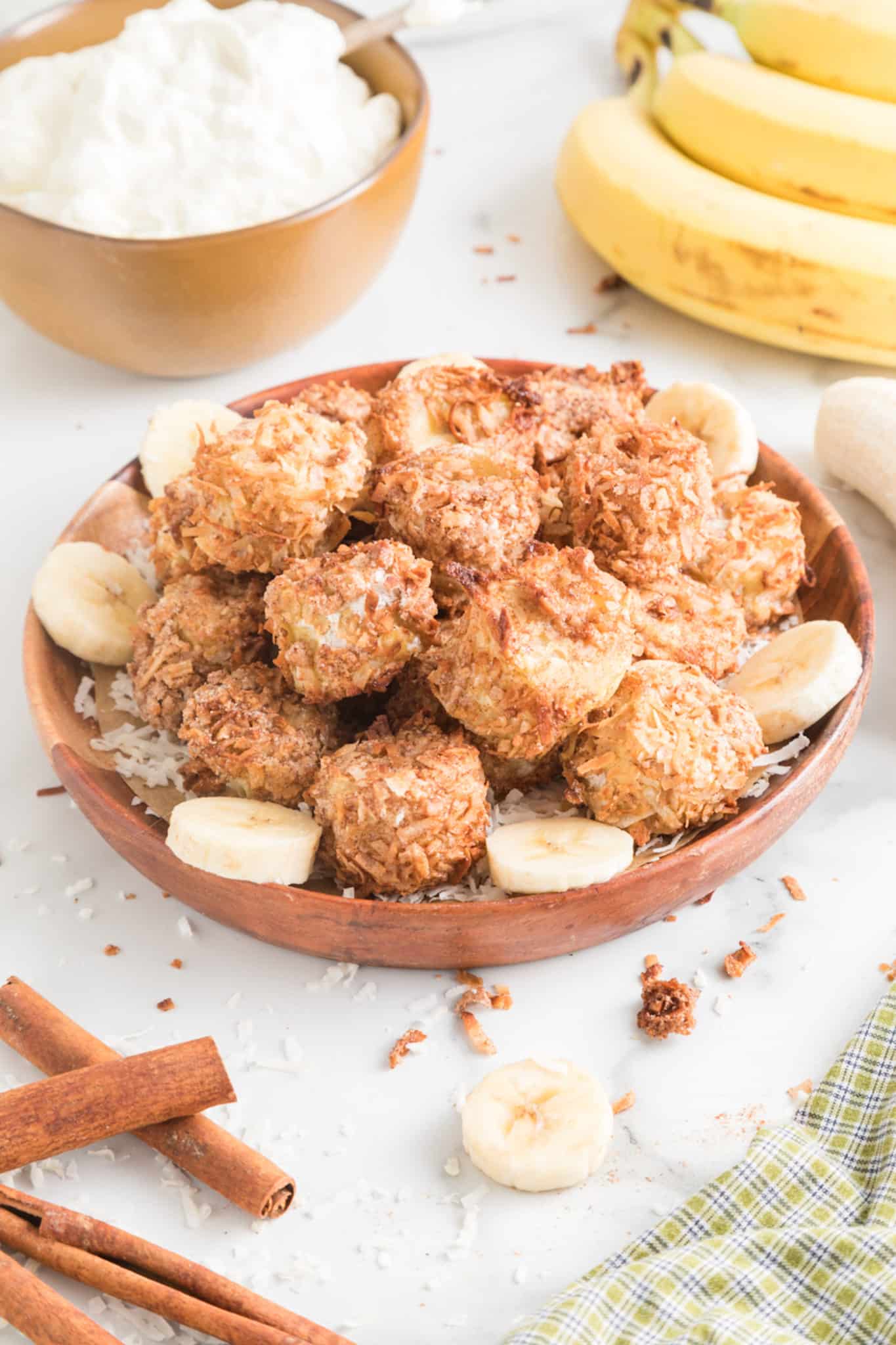 Air fryer banana fritters in a wooden bowl on a white counter.