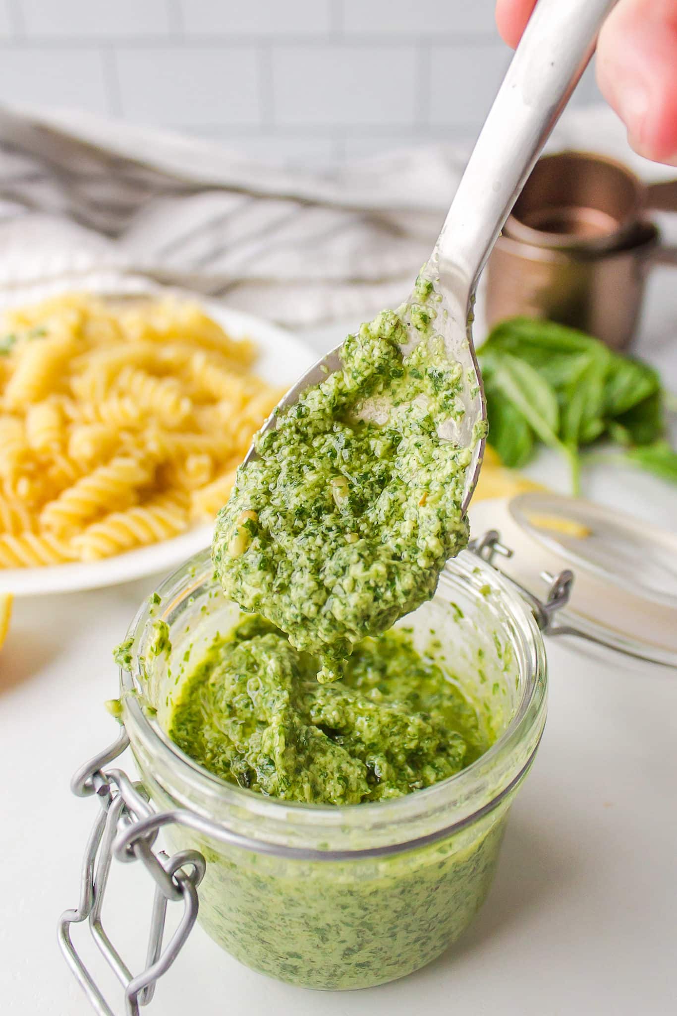 spoonful of vegan pesto sauce getting ready to add to cooked pasta.