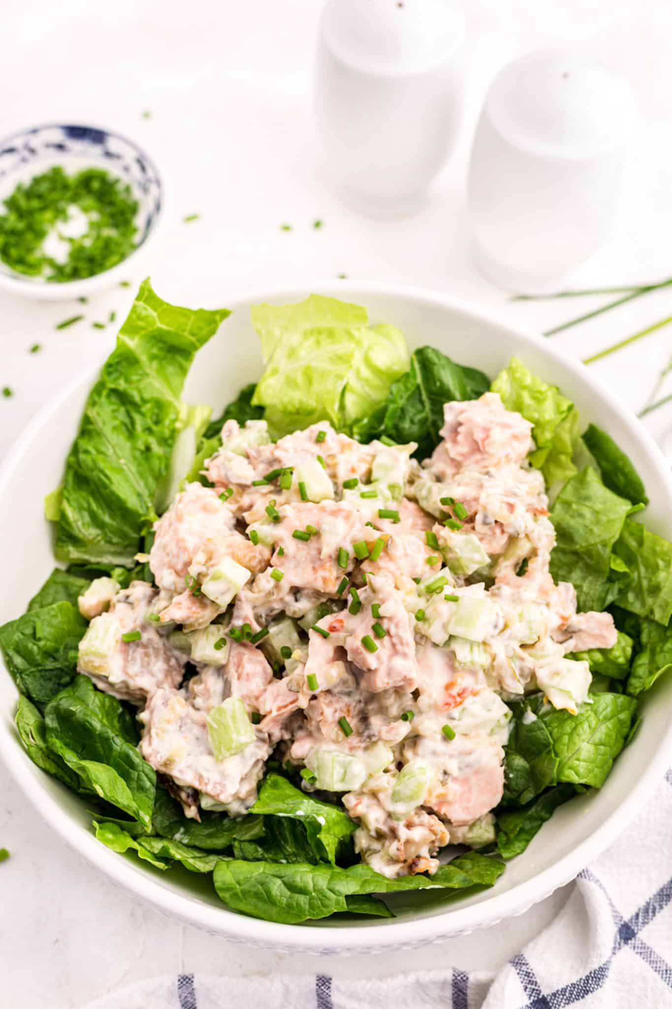 A large white salad bowl filled with greens topped with salmon salad.