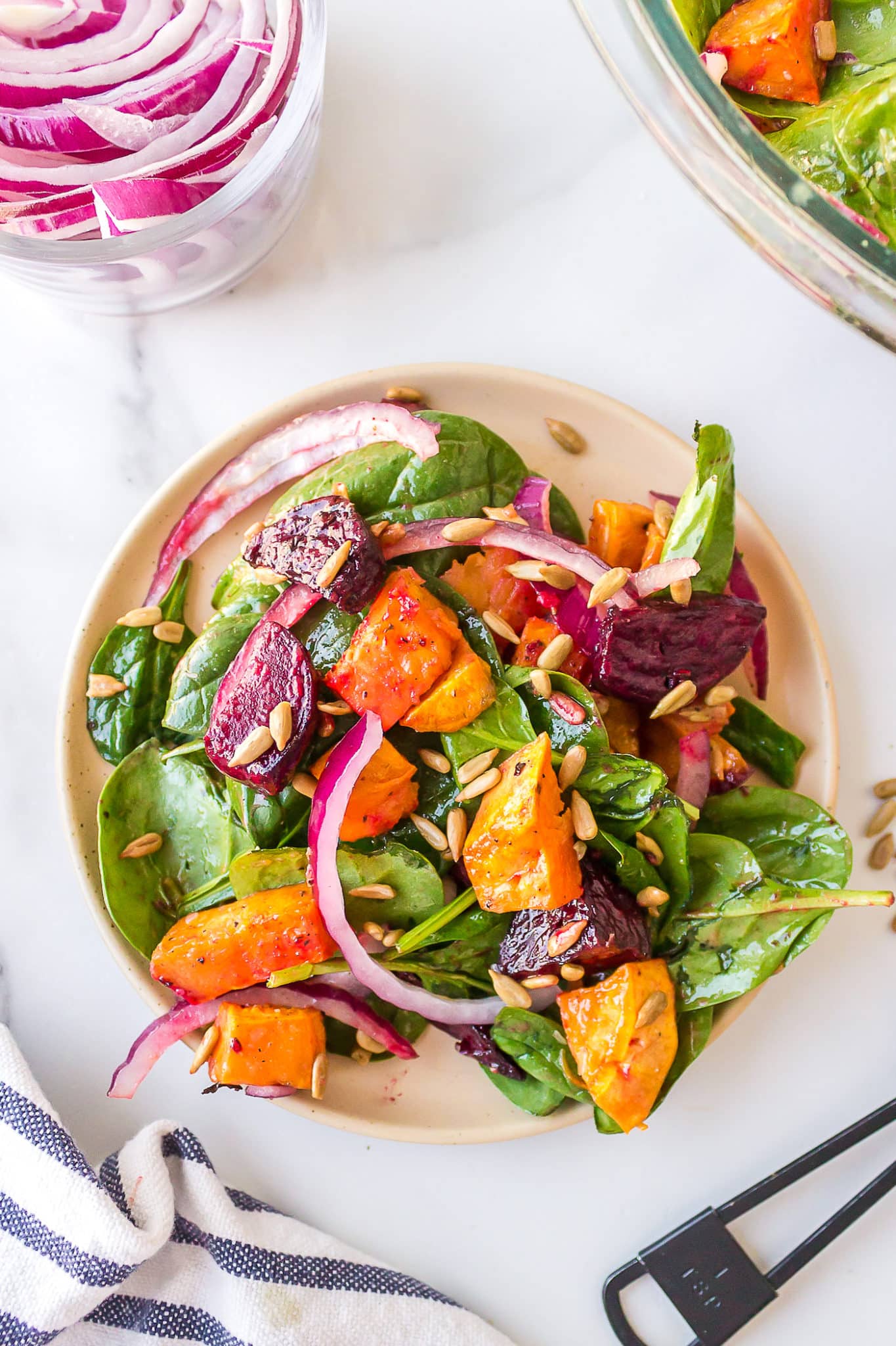 Diced beets and sweet potatoes on a dressed spinach salad on a dinner plate.