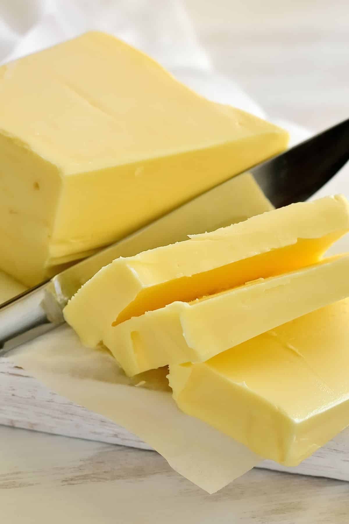 Stick of butter being sliced by a knife on a cutting board.