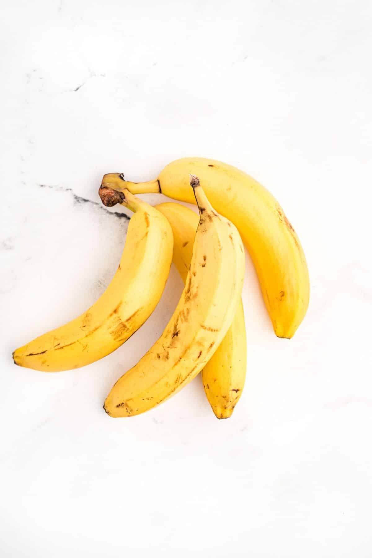 Four ripe unpeeled bananas on a white surface.
