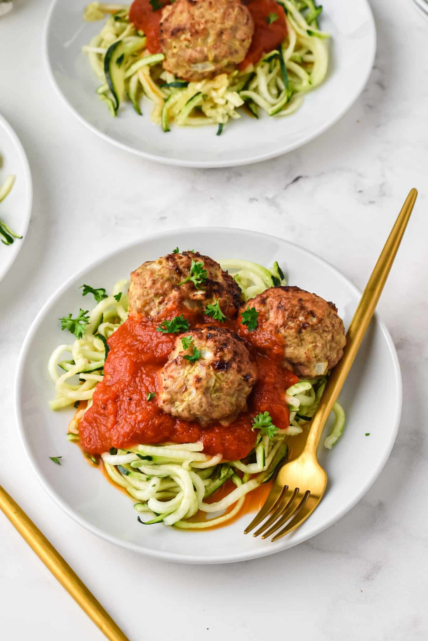 Two plates of zoodles topped with red sauce and turkey meatballs.