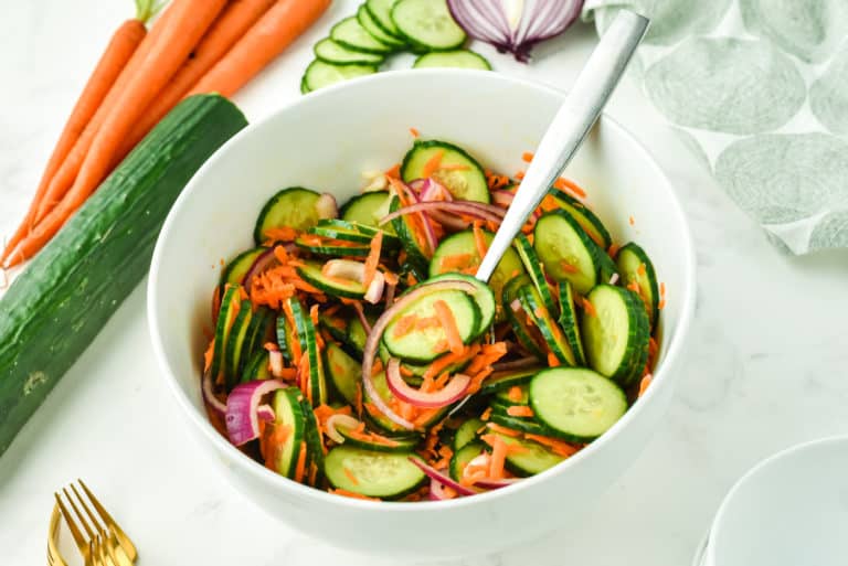 A forkful of cucumber carrot salad over a small white bowl full.