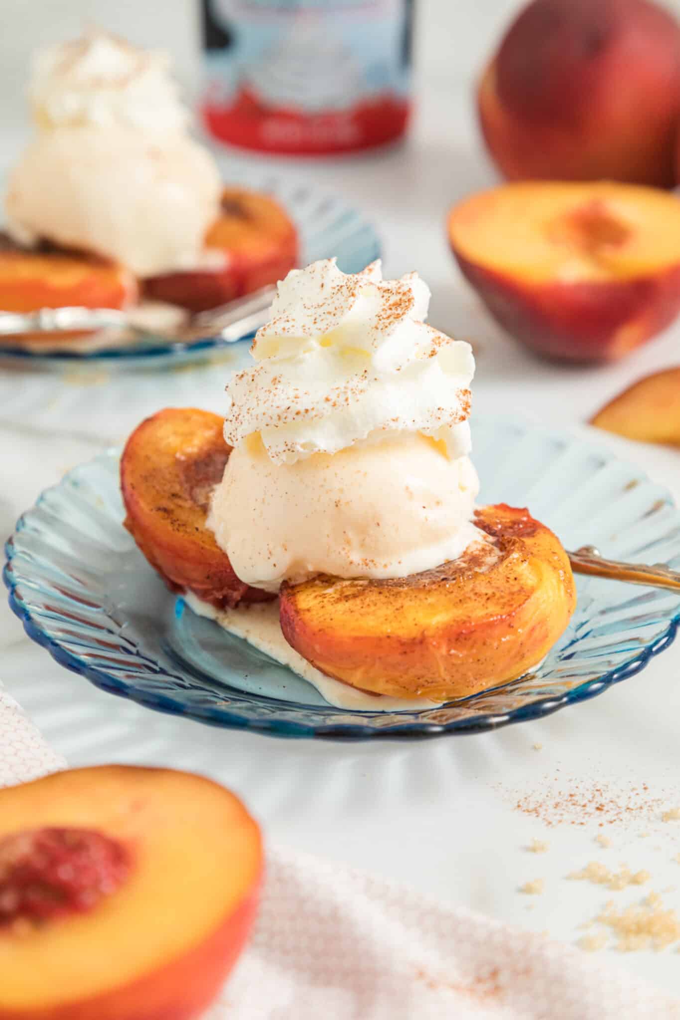 Air fried peach halves on a dessert plate topped with vanilla ice cream.