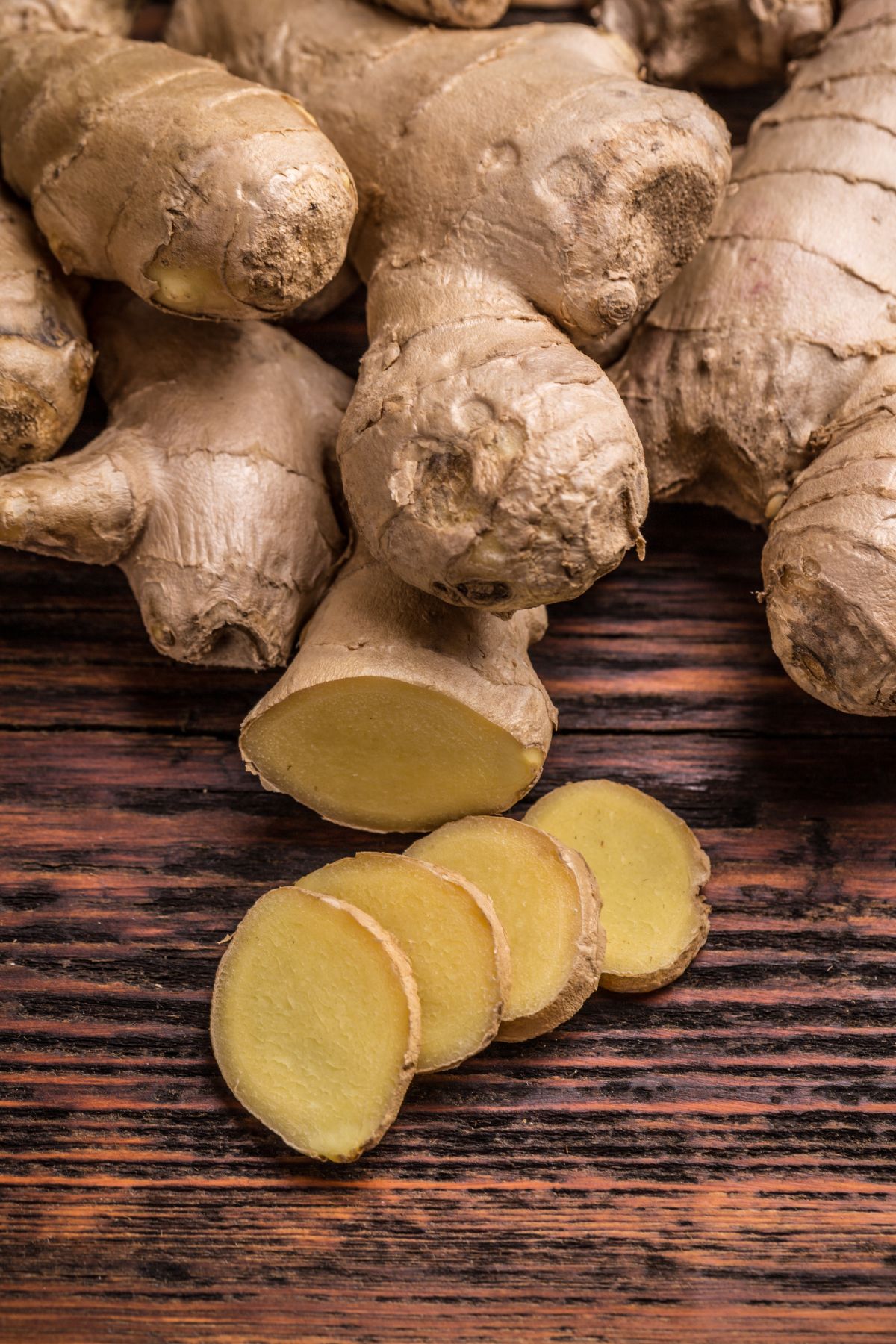 Fingers and slices of ginger root on a wooden surface.
