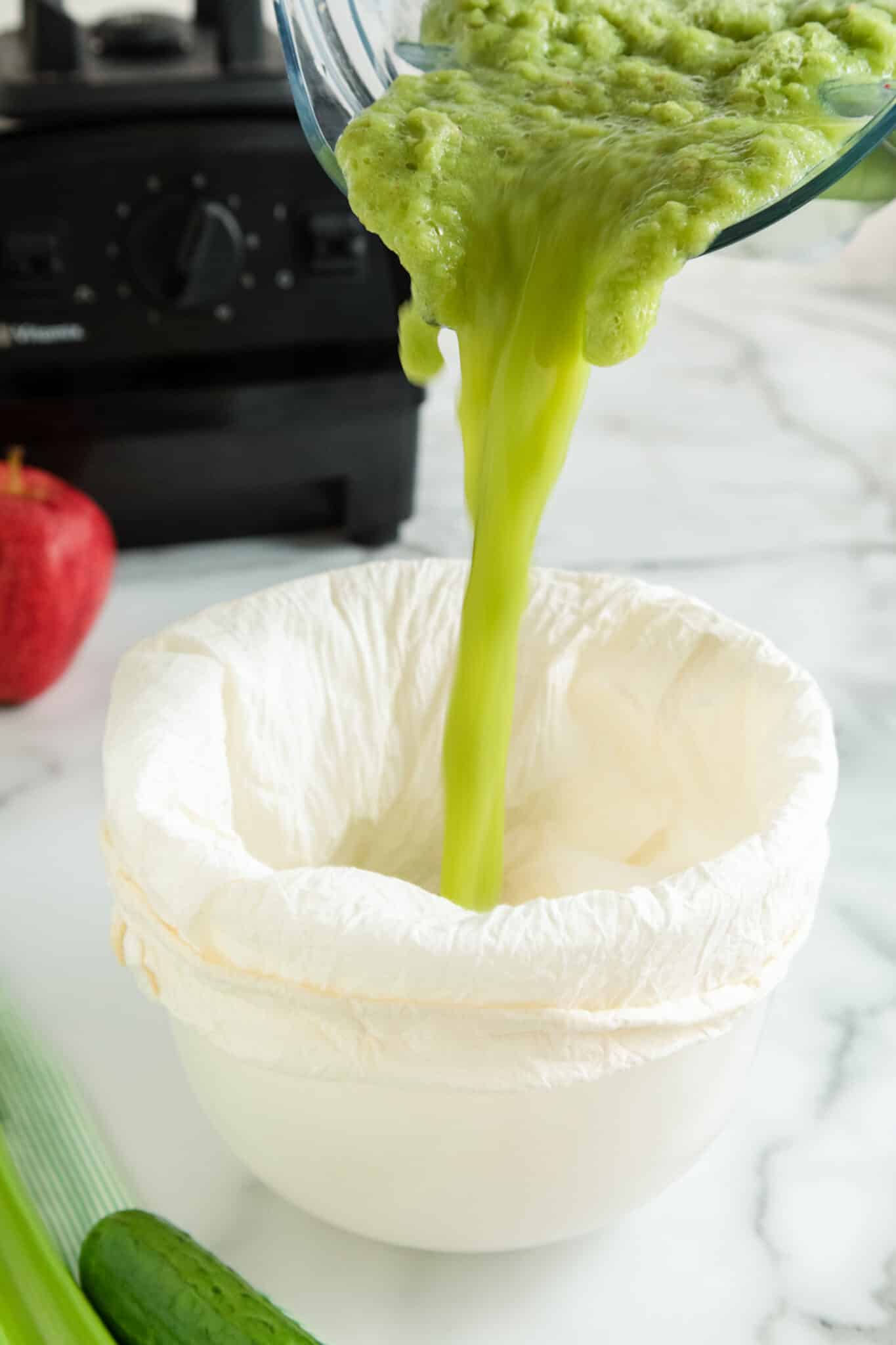 Cucumber celery juice being poured from a blender into a nut milk bag.