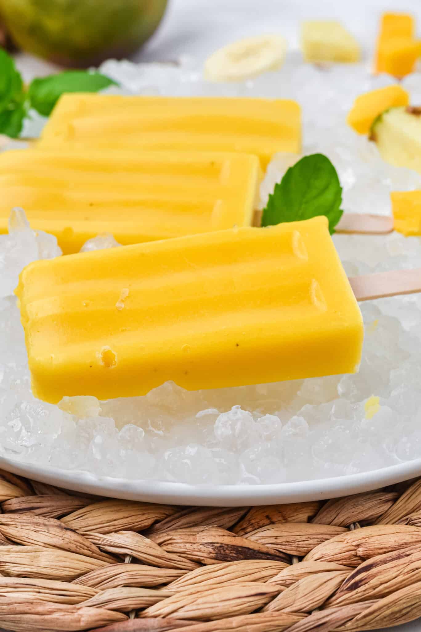 mango popsicles on a plate with ice to keep them cold. 