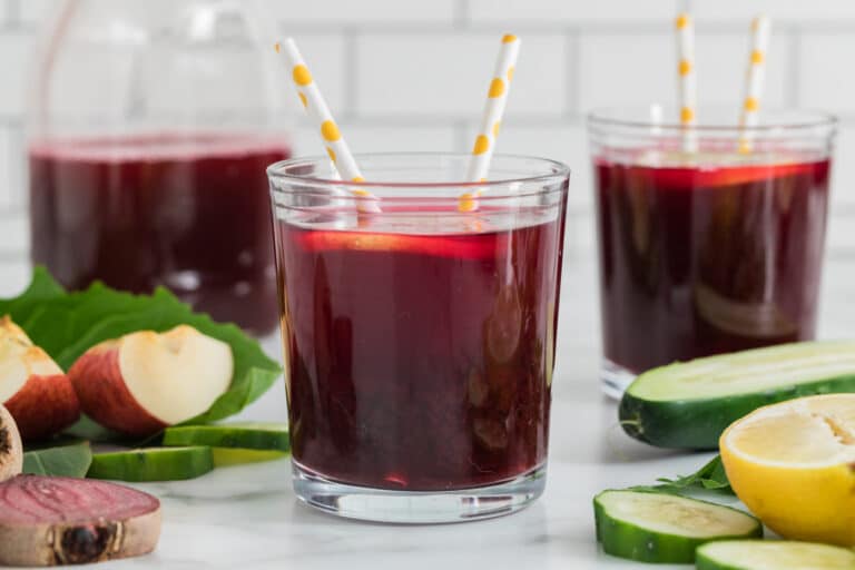 A glass of beet juice with two straws and a lemon slice.