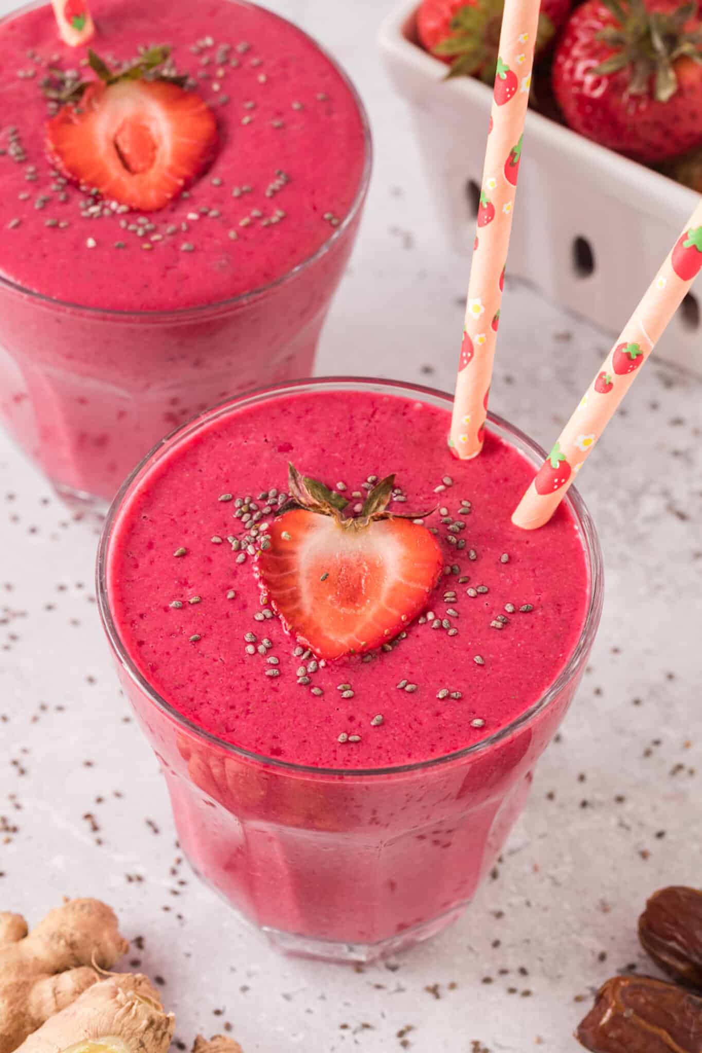 Two pink straws in a glass of strawberry constipation smoothie topped with strawberries and chia.