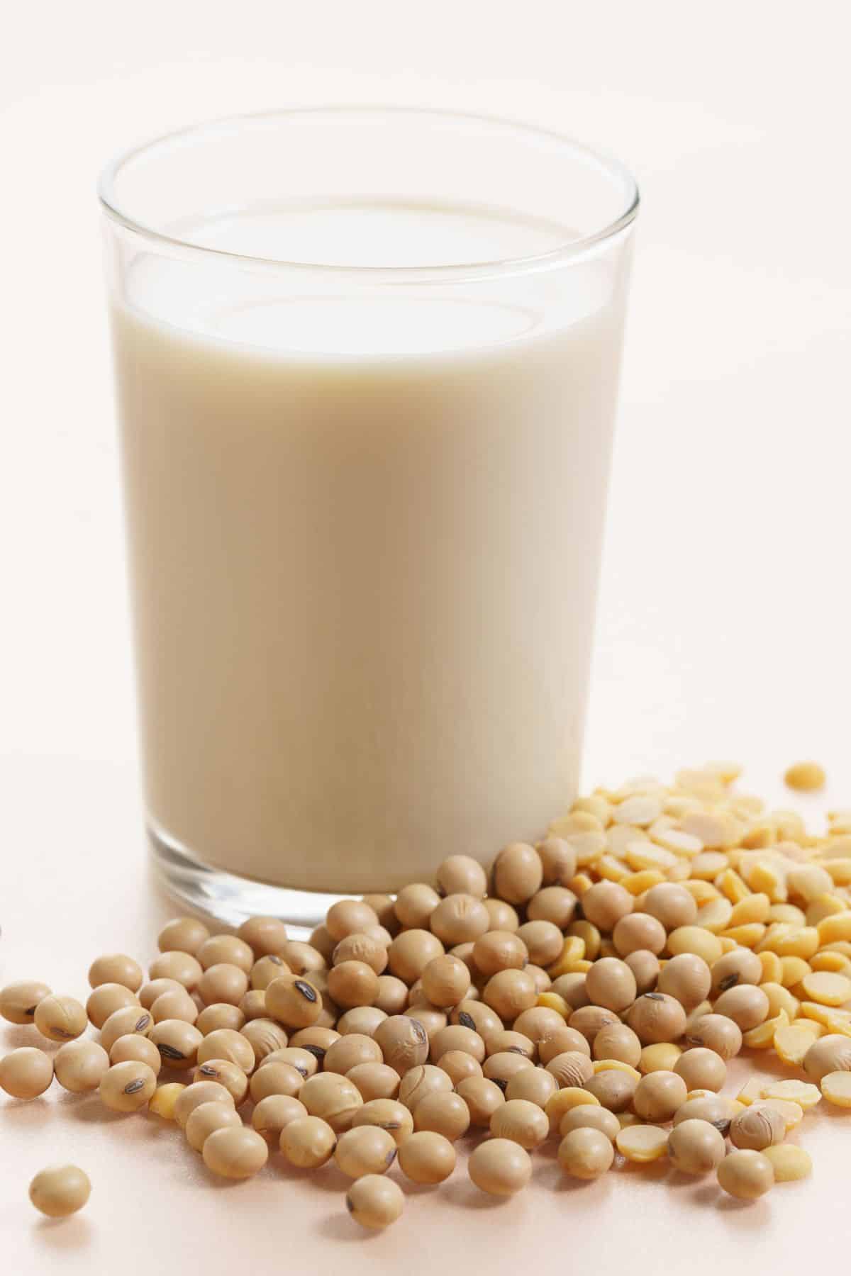 Cup of plant-based milk with dried soybeans on solid surface.