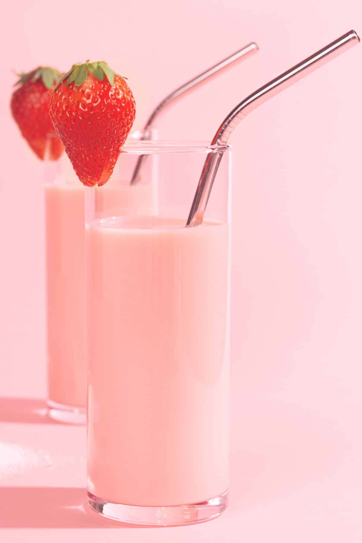 Two tall glasses of strawberry protein smoothies with metal straws.