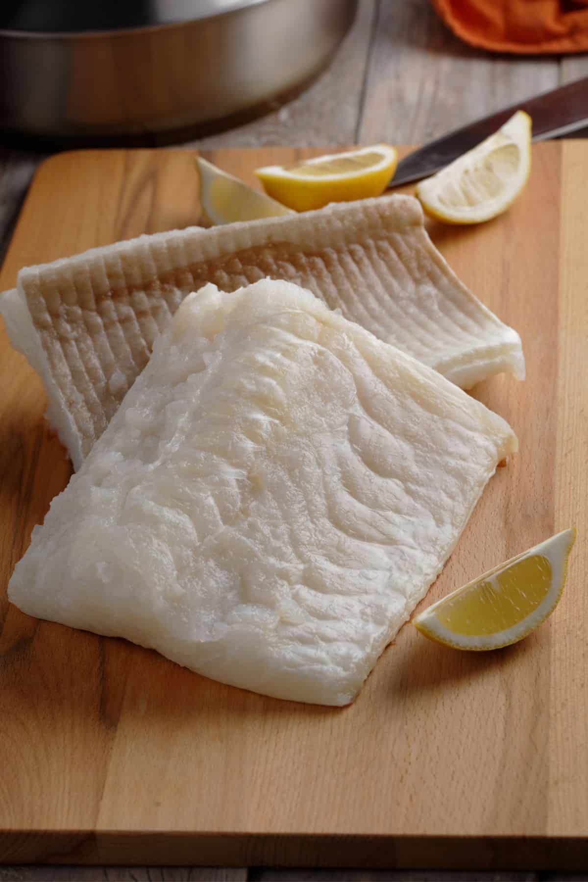 Codfish fillets with lemon wedges on cutting board.