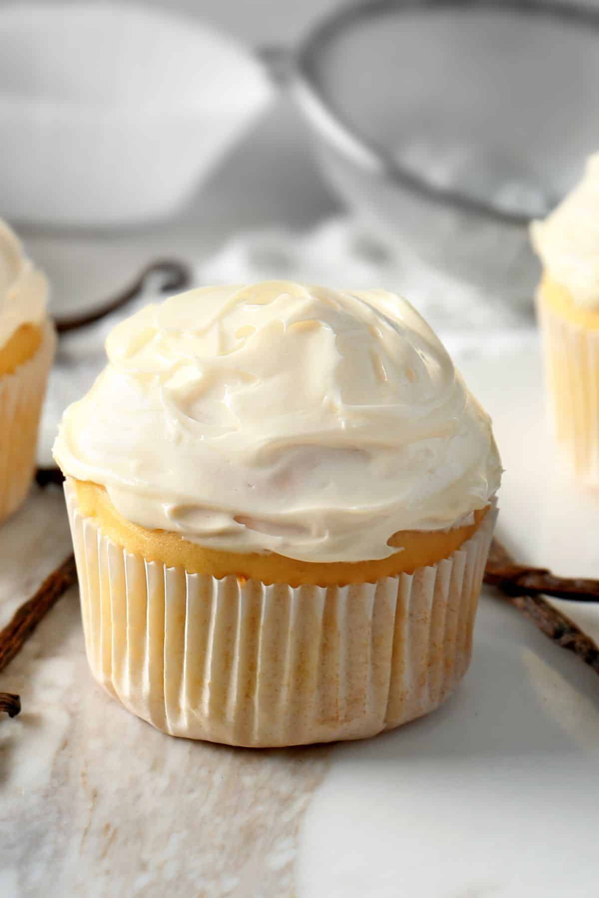 A vanilla cupcake topped with vanilla frosting on a marble counter.