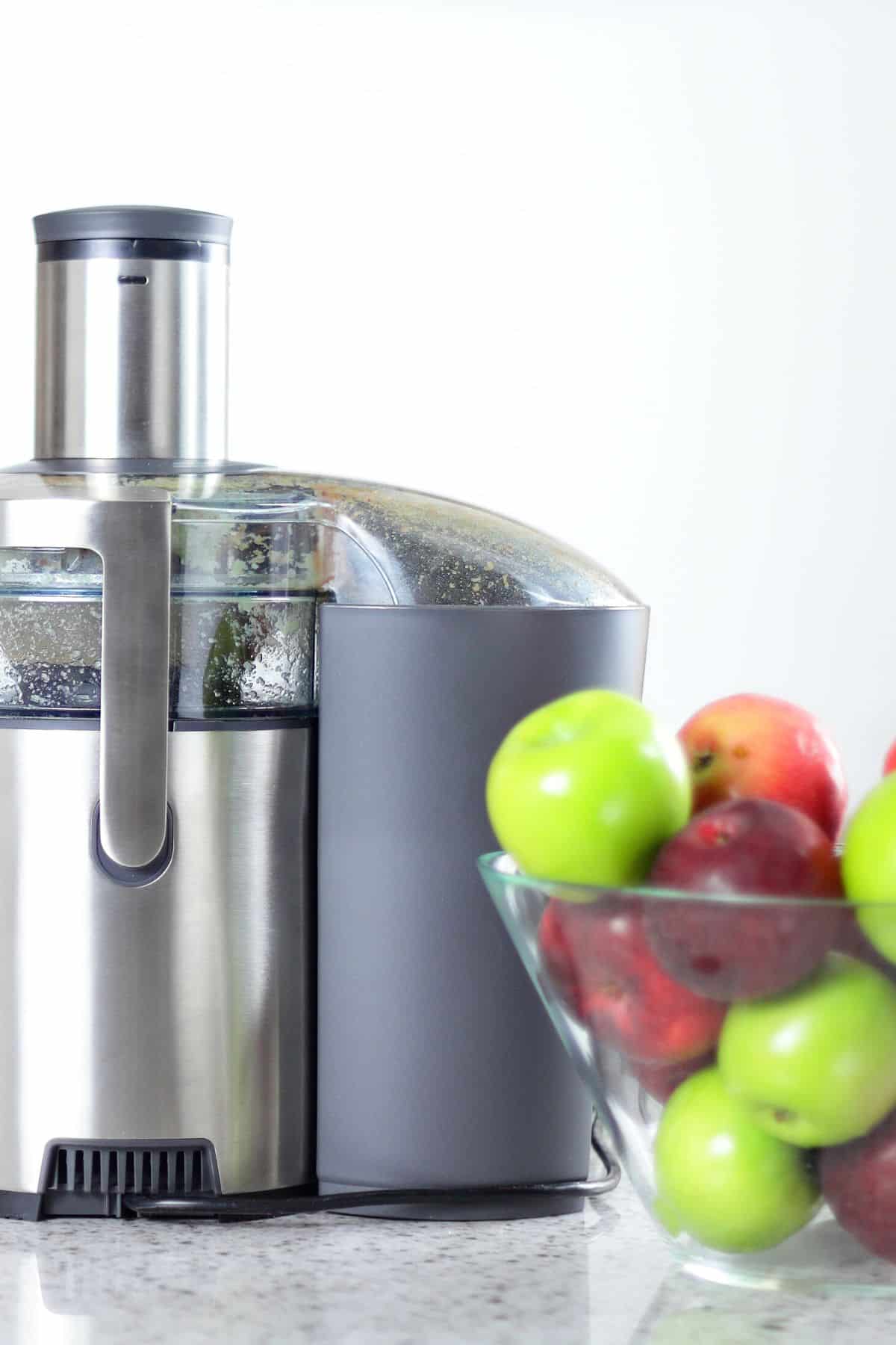 A juicer next to a bowl of red and green apples.
