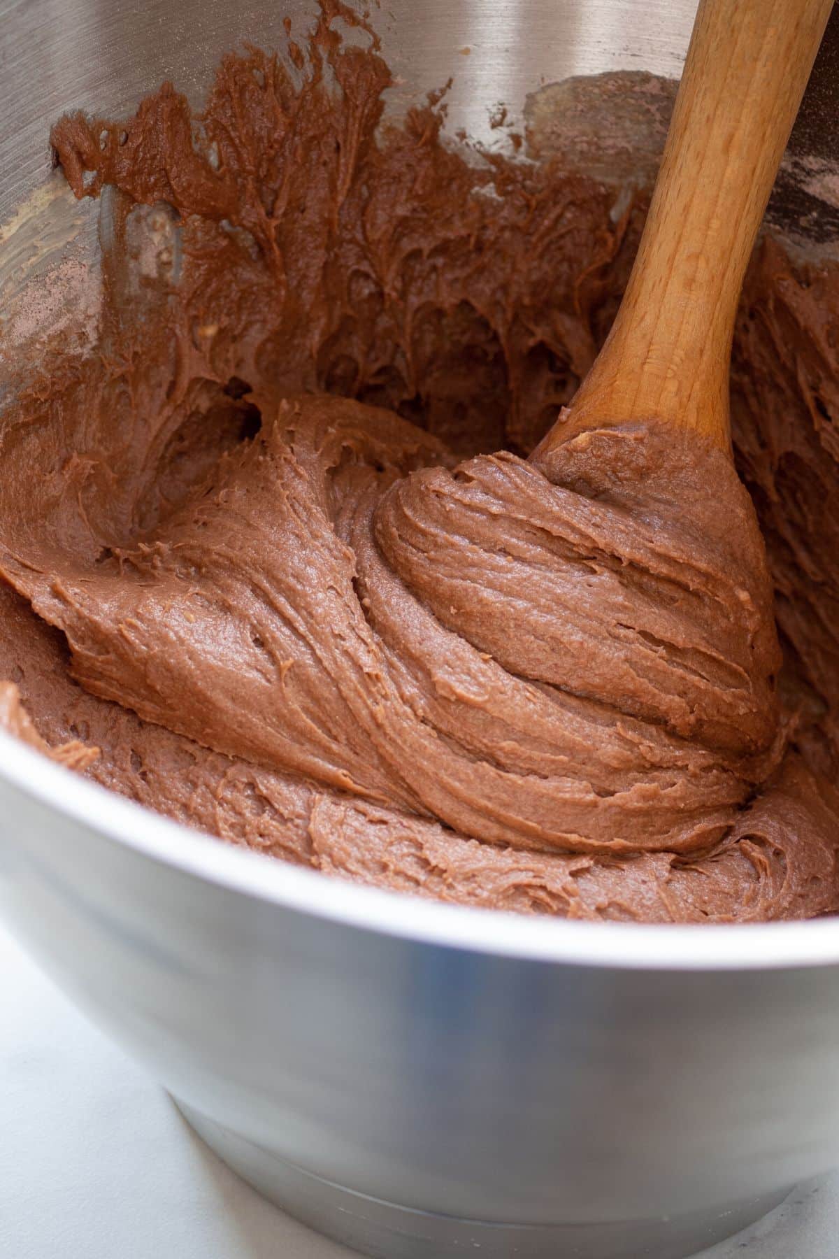 A wooden spoon in a metal bowl of chocolate cake batter.