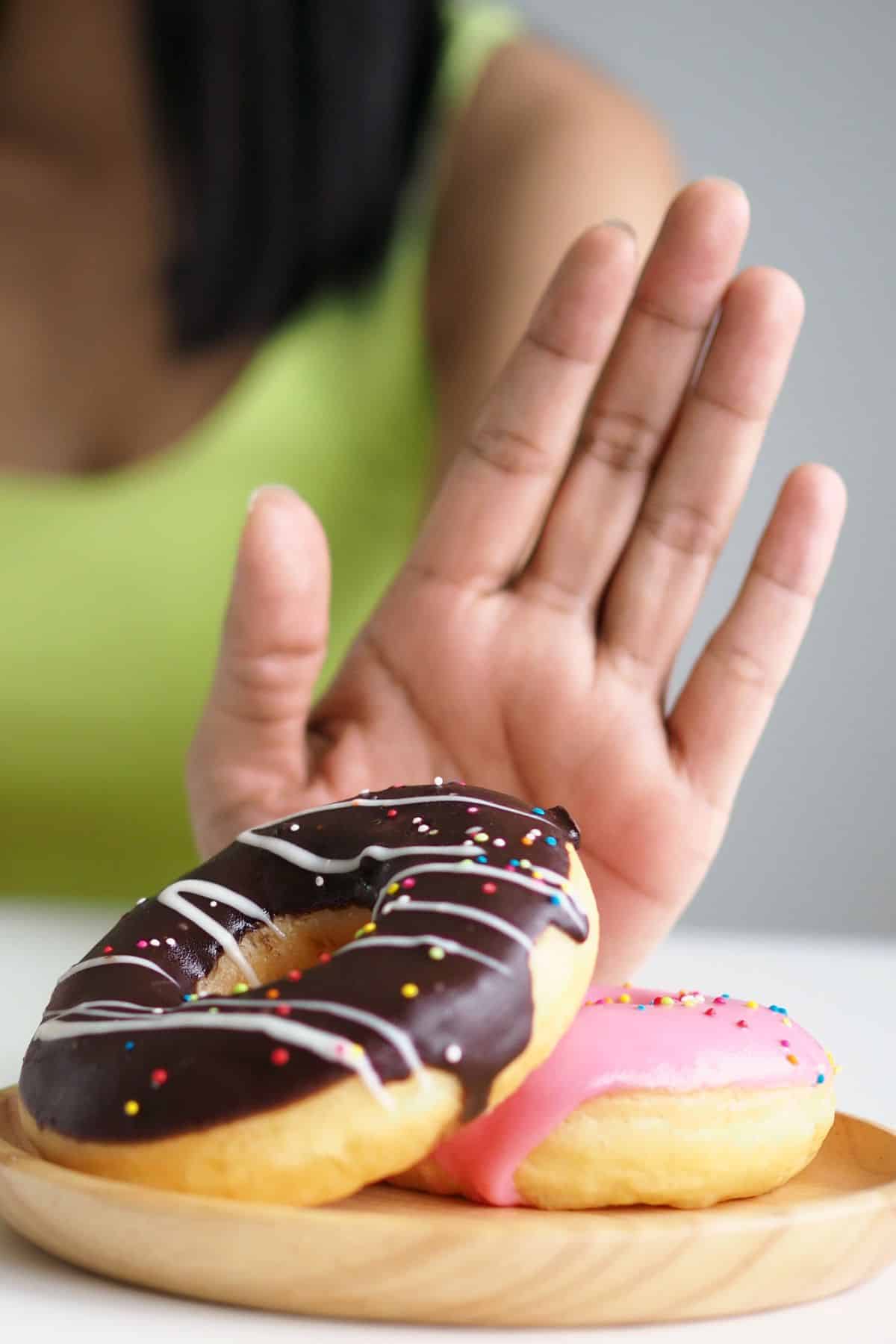 a woman with her hand up in front of a plate of two donuts.