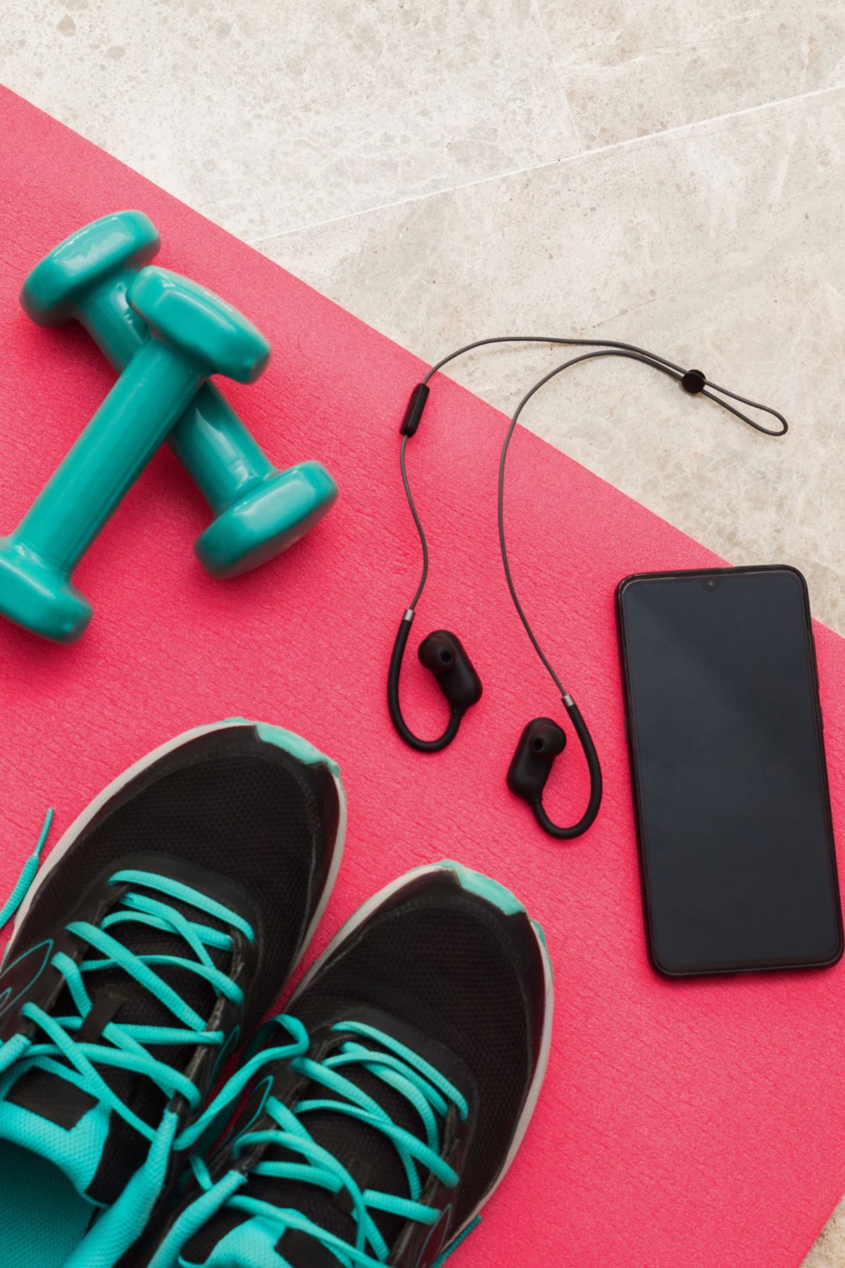 weights, tennis shoes, and a cellphone with ear buds on a yoga mat.