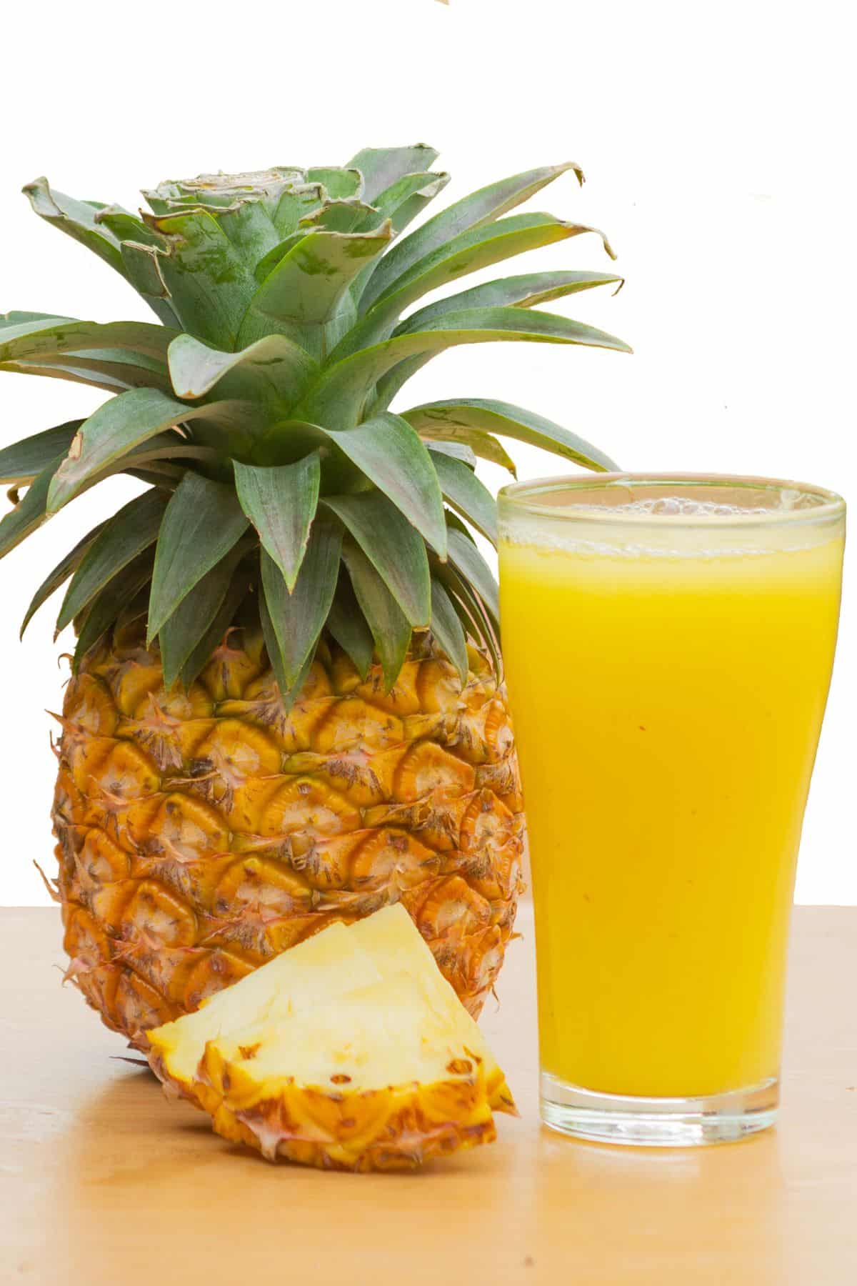 A glass of pineapple juice next to a whole fresh pineapple.
