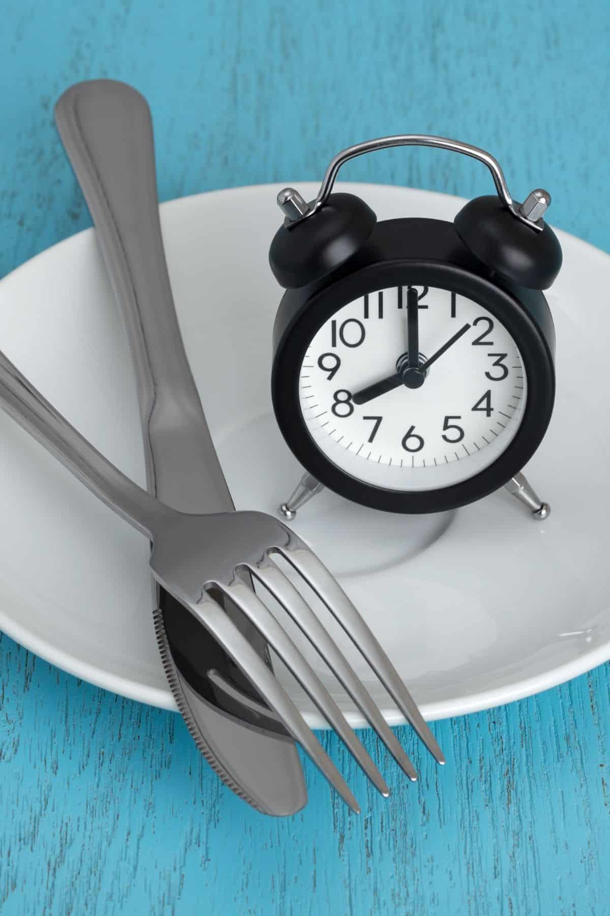 a clock on top of a white plate with a fork and knife.