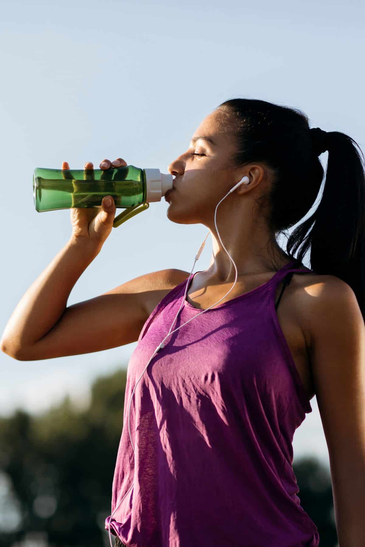 a woman drinking a drink while working out.