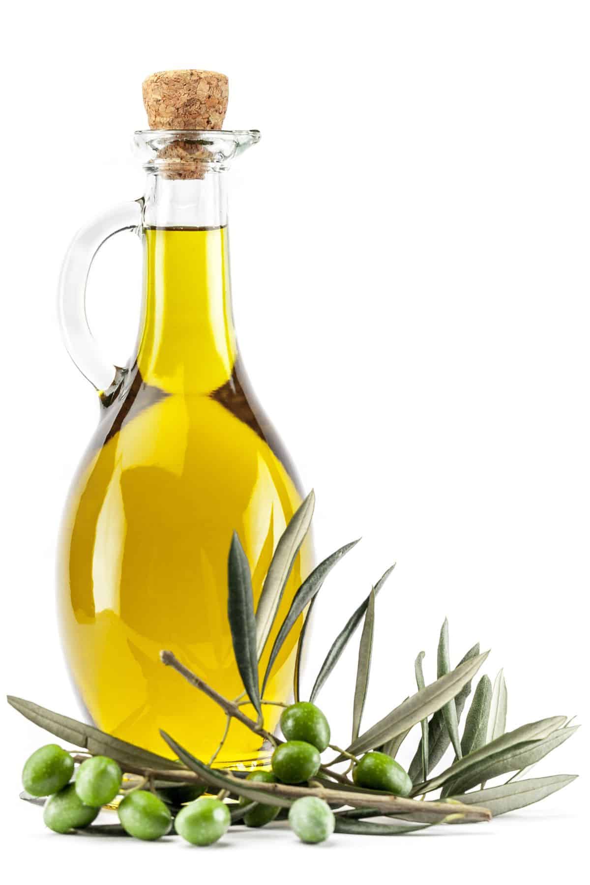 a bottle of olive oil next to a sprig of olives.