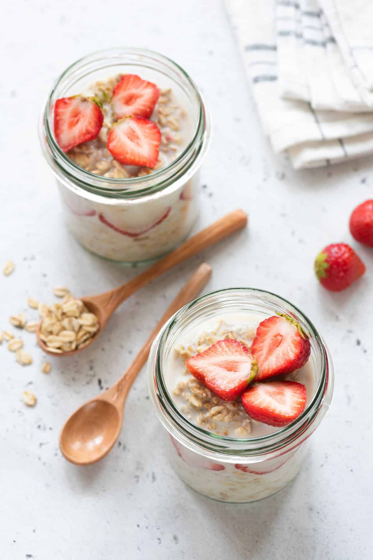 two small jars full of oatmeal topped with strawberries.