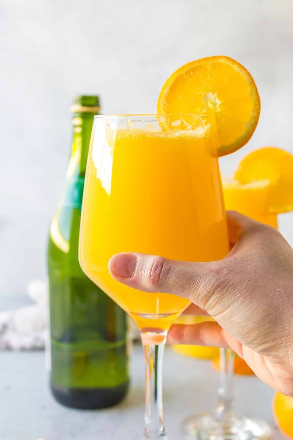 a hand holding a mimosa mocktail.